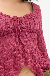 Suur lähivõte isikust, kellel on seljas roosa pitsiline pikakä sleeve crop top, millel on esikinnitus ja rippuvad servad.