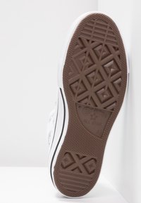 Sole of a white Converse All Star sneaker with brown patterned rubber tread and size 42 markings, angled against a white surface.