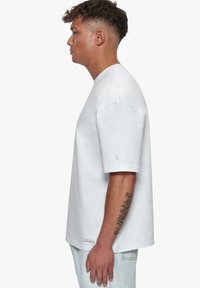 Hvid bomuld t-shirt med afslappet pasform, korte ærmer og broderet logo på ærmet. Enkelt design uden mønstre.