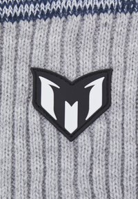 Tessuto grigio lavorato a maglia con una texture a coste, caratterizzato da una toppa logo in bianco e nero a forma della lettera 'M' stilizzata.