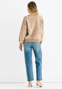 Beige leopard-patterned knit sweater with a relaxed fit, ribbed cuffs, and hem. Paired with light blue straight-leg jeans and beige heels.