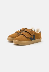 Zapatos de ante marrón con un acabado texturizado, que cuentan con dos correas de velcro, un acento de color azul oscuro y un forro de color crema.
