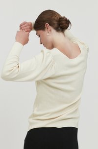 Helle beigefarbene Sweatshirt mit tiefem Rückenausschnitt, gerippten Bündchen und gepufften Schulterdetails. Weiche Textur und figurbetontes Design.