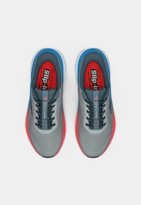 Paire de chaussures de course Skechers grises avec des accents bleus et rouges, des lacets noirs et des semelles intérieures rouges étiquetées « Slip-In Air-Cooled ».