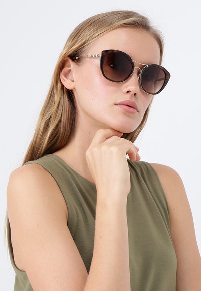 Ochelari de soare cu model țestoasă, cu lentile mari și rotunde, și accente metalice. Montura este lucioasă, având un gradient de la maro închis la maro deschis.