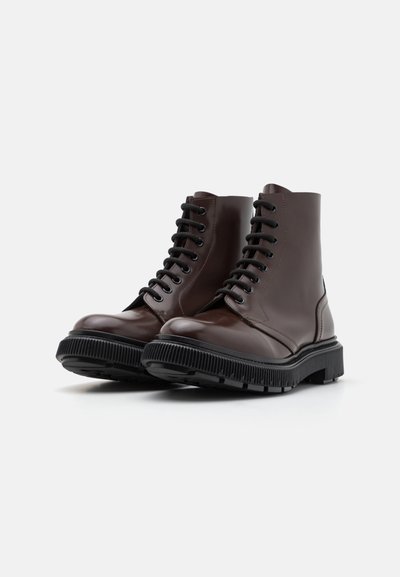 Bottes en cuir marron à la cheville avec semelle en caoutchouc noir texturé, bout rond et lacets. Fini lisse avec un design minimaliste.