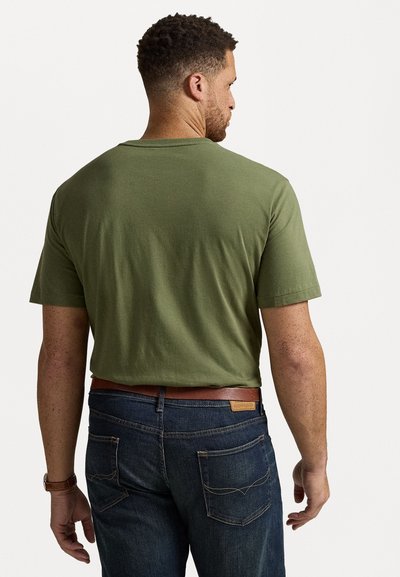 Oliwkowa bawełniana koszulka z krótkim rękawem, zestawiona z ciemnoniebieskimi dżinsami. Dżinsy mają tylne kieszenie z widocznym szwem i brązowy skórzany pasek.