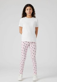 Fehér, rövid ujjú póló, amelyet rózsaszín leggings-szel párosítottak, fekete szív mintázattal. Mindkét ruhadarab laza szabású és puha tapintású.