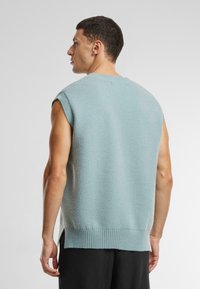 Ärmeloser, lyseblå strikket sweater med ribbet kant og sideslids, der har en blød tekstur og afslappet pasform.