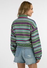Multikleuren patroonjas met groene, roze en blauwe strepen. Gemaakt van een gestructureerde stof met een hoge kraag en een elastische taille.