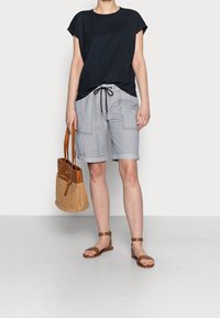 Námořnický top s krátkým rukávem, světle šedé krátké kalhoty s kapsami, hnědé sandály s řemínky a béžová pletená kabelka s koženými akcenty.