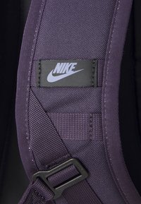 Correia de tecido roxa da Nike com um patch de logotipo preto, costura reforçada e uma fivela de plástico. A textura parece durável e suave.