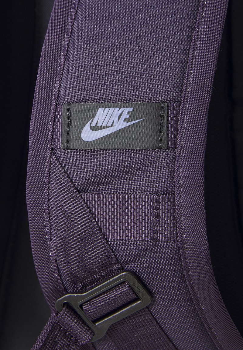 Sangle en tissu purple de Nike avec un patch logo noir, coutures renforcées et une boucle en plastique. La texture semble durable et lisse.