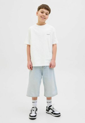 Witte katoenen t-shirt met korte mouwen en een logo, gecombineerd met lichtblauwe denim shorts en zwart-witte sneakers met accenten.