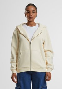 Crème kleurige zip-up hoodie met een grote capuchon, voorzakken, geribbelde manchetten en een relaxte pasvorm. Draag het over een wit T-shirt en combineer het met blauwe broek.