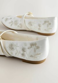 Balerini din satin alb, cu modele florale brodate în argintiu și bej. Au vârful rotund și o talpă joasă, maro, cu baretă.