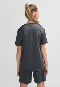 Graues Sport-T-Shirt mit kurzen Ärmeln, aus leichtem Material. Hat ein schlichtes Design und ein Logo auf den Shorts. Glatte Textur.