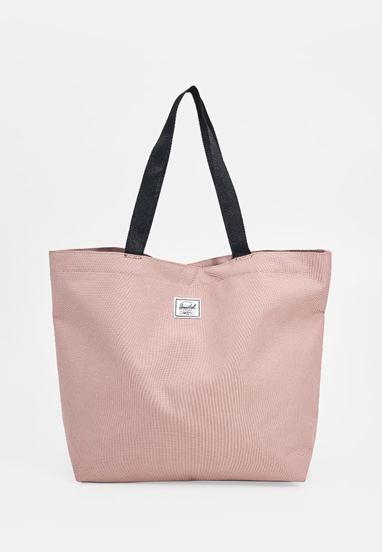 Borsa a tote di stoffa rosa con manici neri, caratterizzata da un'etichetta con logo quadrato. Texture morbida e design spazioso, adatta per l'uso quotidiano.