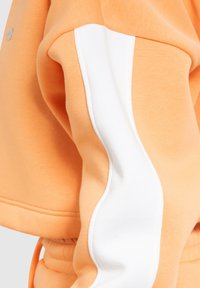 Oranje sweatshirt met een witte zijstreep, gemaakt van zacht katoen. De mouwen hebben een gathered, elastische afwerking voor een snug fit.