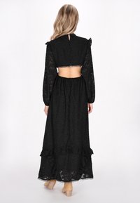 Rochie neagră, cu mâneci lungi, cu spatele scurtat și tiv volanat. Confecționată dintr-un material transparent cu un model floral subtil și închidere cu nasturi.
