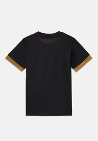 Fekete hálós rövid ujjú póló. Az ujjakon arany díszítések találhatók, amelyek kontrasztot alkotnak a fő anyag textúrájával.