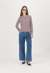 Camisa de rayas rojas y blancas de manga larga con escote redondo, combinada con pantalones vaqueros de pierna ancha en azul y zapatos de tacón negros.