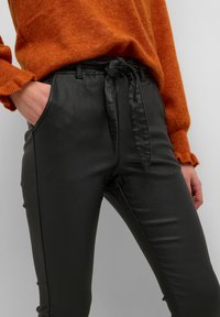 Svarta byxor i fake läder med dragsko framtill, slim fit, sidfickor och kontrasterande sömmar, tillsammans med en orange tröja.