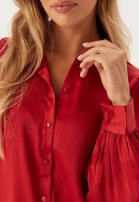Rode button-up shirt met een geplooide textuur, met lange, geraffineerde mouwen en ronde knopen langs de sluiting. Soepele stofafwerking.