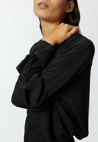 Blusa nera leggera con un fit rilassato, dotata di maniche a sbuffo e piccoli bottoni lungo i polsi. Texture liscia e design minimal.