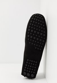 Semelle de chaussure en daim noir avec des grips en caoutchouc ronds et surélevés, disposés en grappes au niveau du talon et de l'avant.