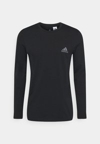 Musta pitkähihainen t-paita, joka on valmistettu puuvillasta. Siinä on pyöreä pääntie ja pieni harmaa Adidas-logo vasemmassa rinnassa. Tasainen pinta.