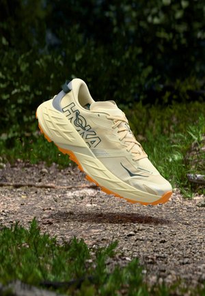 Világos sárga futócipő texturált felsőrésszel, szürke részletekkel és narancssárga talppal, párnázott kialakítással a tapadás érdekében.