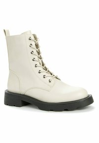 Botines de cuero beige con puntera redonda, ocho ojales metálicos y suela de goma negra. Incluyen una lengüeta en la parte trasera para facilitar su puesta.