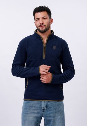 Pull-over en polaire bleu marine avec un zip mi-hauteur et des accents vert olive. Il présente un logo sur la poitrine et un tissu texturé. Manches longues, coupe décontractée.
