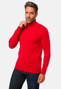 Roter Rollkragenpullover in einem figurschmeichelnden Strickdesign, mit langen Ärmeln und einem gerippten Kragen. Kombiniert mit dunkelblauen Jeans. Weiche Textur sichtbar.
