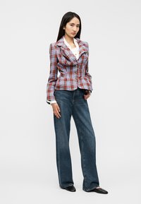 Καρό σακάκι σε κόκκινο, μπλε και άσπρο με δομημένους ώμους, τρία κουμπιά και μέση με πεπλούμ, συνδυασμένο με σκούρα μπλε τζιν φαρδιάς γραμμής.