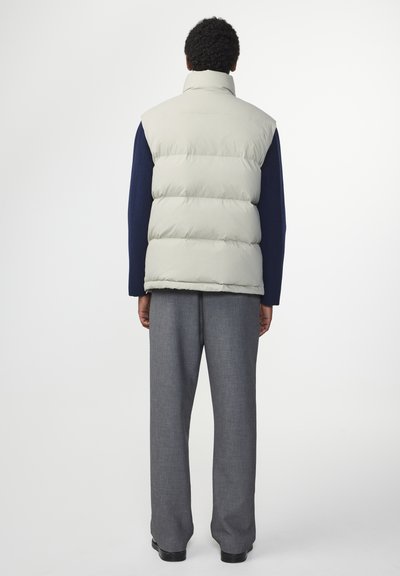 Vatteret, lys grå vest med høj krave, båret over en marineblå sweater. Sammen med grå skræddersyede bukser og sorte sko.