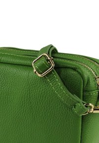Groene leren handtas met een getextureerd oppervlak, gouden hardware-accenten en een ritsluiting. Gestikte details op de riem en randen.