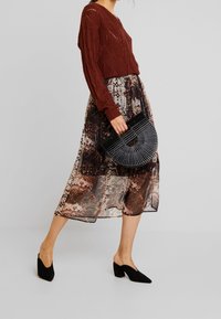 Maroon knitted sweater, patterned midi skirt in brown tones, black pleated handbag, and black mules with a block heel.