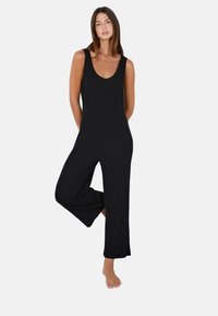 Mono negro de canalé con escote redondo, piernas anchas y un cuerpo ajustado. Textura suave, diseño sin mangas y corte hasta el suelo.