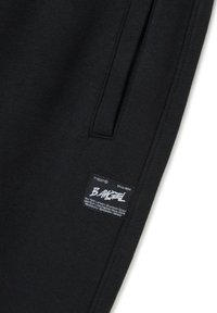 Schwarze Jogginghose aus einem Baumwollmischgewebe. Mit einer Seitentasche und einem markierten Stoffetikett mit weißem Text und Stadtnamen.