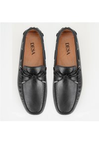 Zwarte leren loafers met een gladde textuur, voorzien van veters en metalen details. De binnenzool is bruin met "DESA" erin gedrukt.