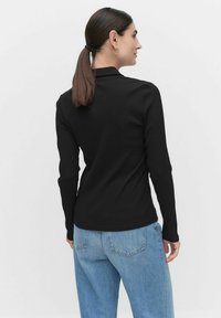 Musta ribbikuvioitu pitkähihaine paita korkealla kauluksella, yhdistettynä vaaleansinisiin korkeavyötäröisiin farkkuihin, nähtynä takaa.