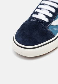 Marineblå pigmentert sneaker med hvite snører, som har en blå og hvit mønstret sidepanel og en teksturert gummisåle med svarte detaljer.