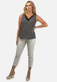 Czarny i biały top w kropki bez rękawów z dekoltem w serek wykończonym koronką, w połączeniu z jasnobeżowymi spodniami typu cropped i złotymi sandałami na koturnie.