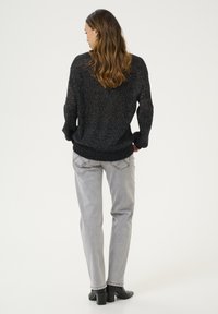 Svart texturerad stickad tröja med lös passform och ribbad kant, tillsammans med ljusgrå raka jeans och svarta klackade ankelstövlar.