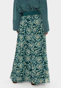Blomster maxi-sukker i mørkegrøn stof med lys blomster mønster og gule accenter. Har en elastisk talje og et let og flowy design.