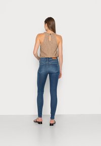 Top halter de rayas marrones con espalda con abertura, combinado con jeans skinny de tiro alto azul y sandalias negras, visto desde atrás.