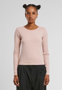 Long-sleeve pink cotton shirt with a round neckline. Smooth texture, fitted design, and minimal stitching details. Paired with black pants.