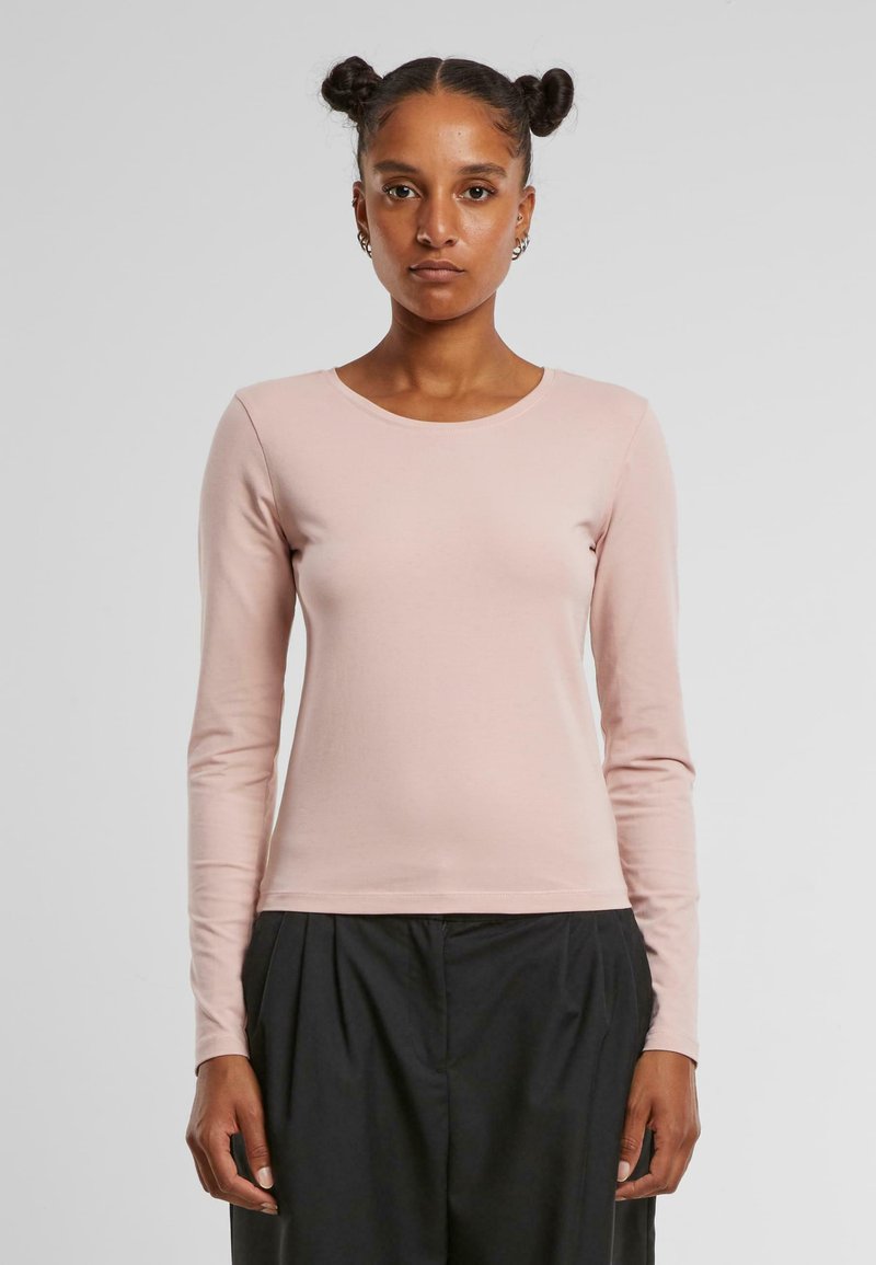 Long-sleeve pink cotton shirt with a round neckline. Smooth texture, fitted design, and minimal stitching details. Paired with black pants.